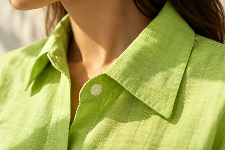Enquadramento aproximado da gola, do botão e da textura nítida do tecido de uma camisa verde-limão